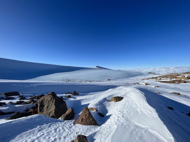 Snowy ridges with exposed rocks and blue sky.