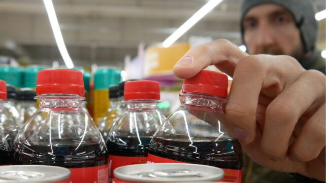 Close-up of a male buyer's hand taking a plastic bottle of cola from a supermarket shelf