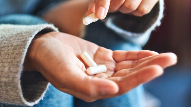 Closeup image of a woman holding and picking white medicine capsules in hand