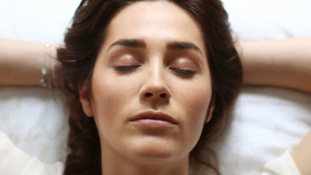Close up on face of a young brunette woman with closed eyes, lying on a white pillow