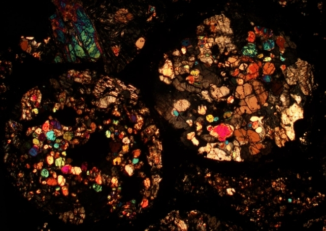 Reflective blobs of bright colors showing meteorite composition from thin slices under a microscope