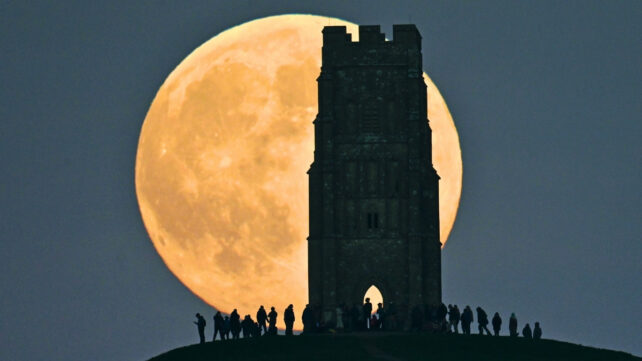 People (in silhouette) gather to watch the moon rise over the Glastonbury Levels