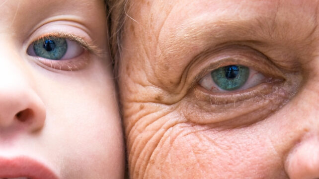 Close up showing the eyes of a young child and an elderly person, with their faces pressed side to side