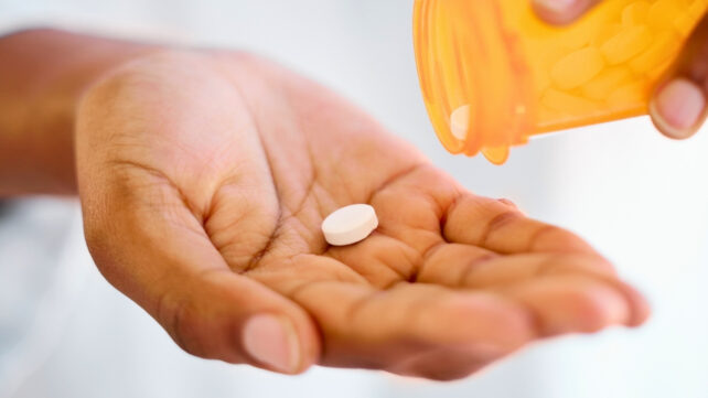 hand holding a pill, with another pill pouring from an orange prescription jar
