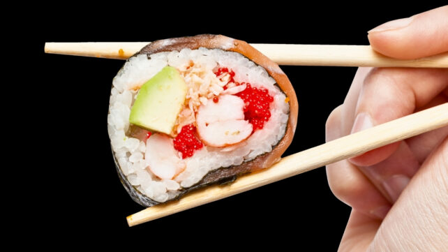 Hand holding chopsticks with avocado and seafood sushi