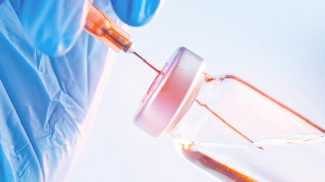 Blue-gloved hand holding a syringe and drawing up liquid from a vial