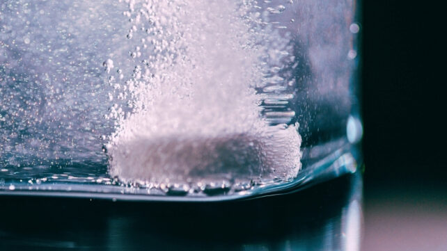 Tablet in glass with water on a black background
