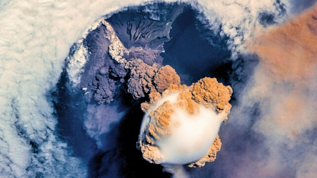 Volcano eruption seen from space, showing a huge white blob coming out of a crater