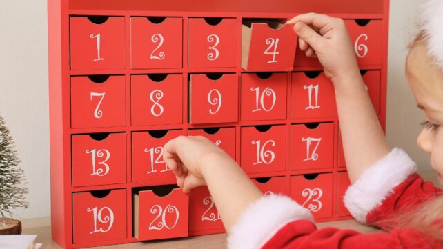 Child in christmas outfit opening advent calendar drawers