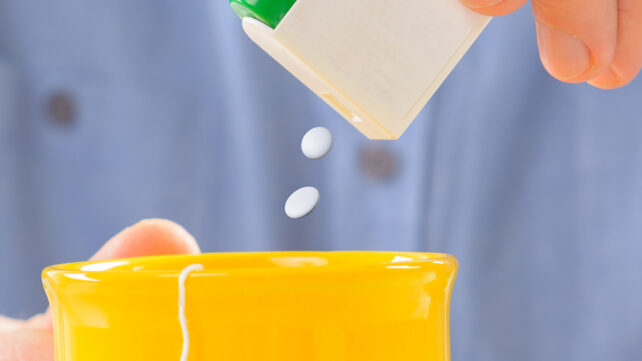 Sweetener tablets and hand with box whit cup of tea