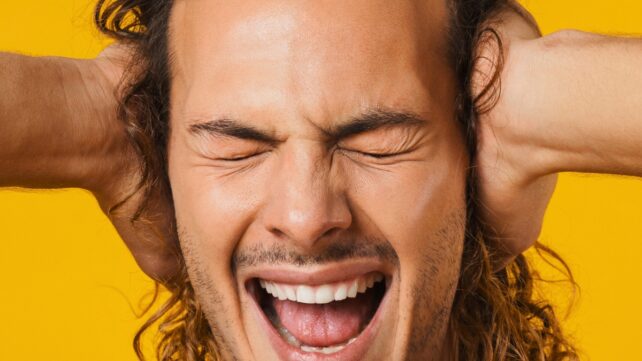 Close up of frustrated brunette man holding hands over his ears