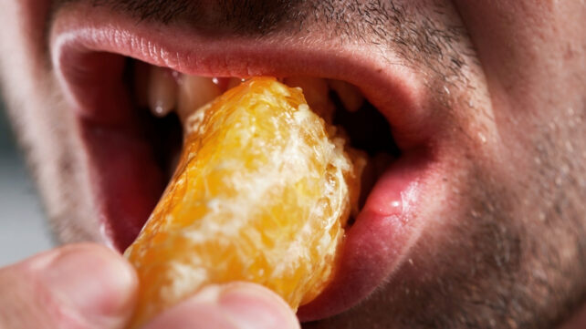 High resolution close-up image of a person's mouth, eating a segment of mandarin
