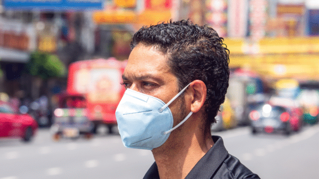 Man wearing mask standing beside street filled with vehicles.