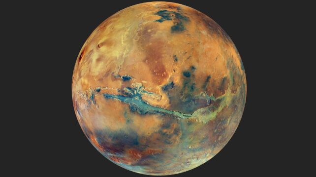 This image shows the globe of Mars set against a dark background. The disc of the planet features yellow, orange, blue and green patches, all with an overall muted grey hue, representing the varying composition of the surface.