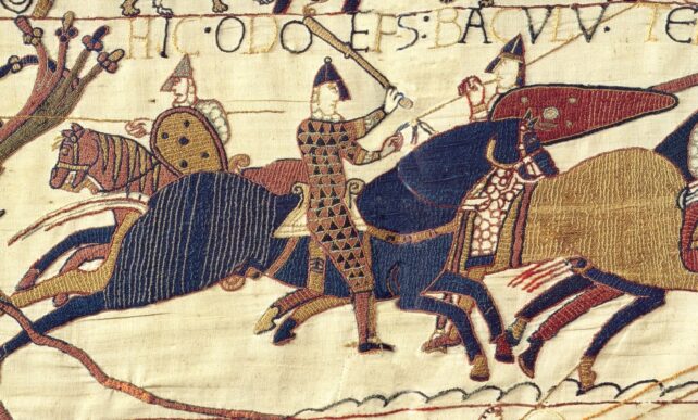 a section of the bayeux tapestry showing a battle scene embroidered in yellow, blue and red, onto a pale cloth background