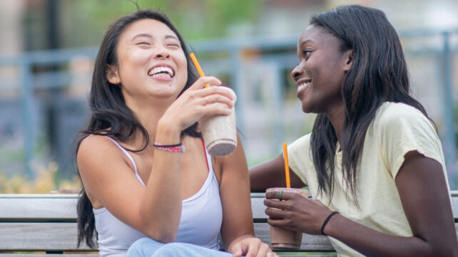 Two young adults enjoying takeaway drinks on a bench outdoors