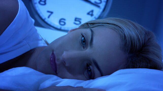 Woman awake in bed, with a clock showing 3 am in the backgound
