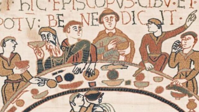 a section of the bayeux tapestry depicting six men around a crescent table eating and drinking. a man below serves wine.