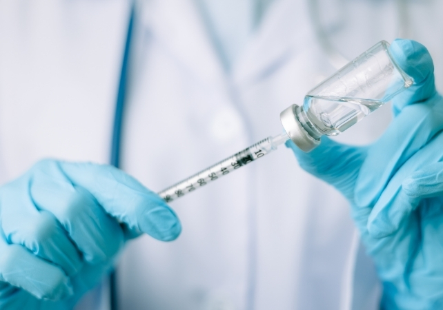 person with blue gloves filling a hypodermic syringe from a vial
