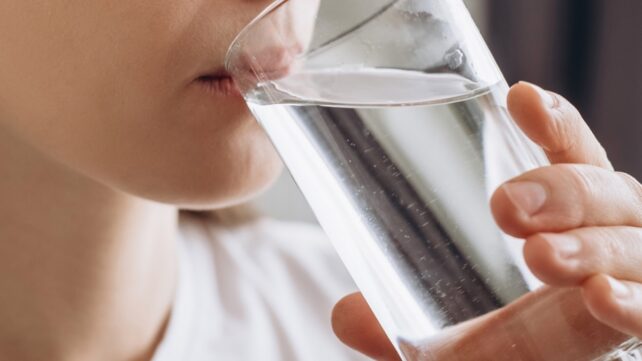 Side view close up of a young person drinking water from a glass