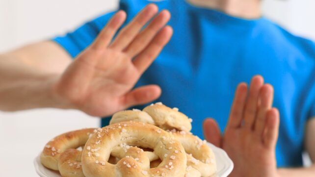 Person's hands raised in front of a plate of pretzels, as if to decline the offer