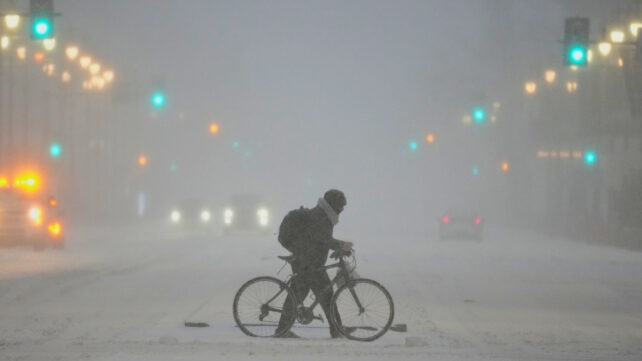 Person pushes a bicycle across a stormy winter street