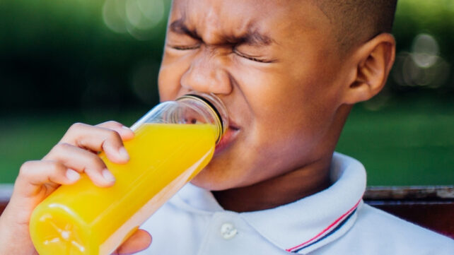 boy pulling a face while drinking orange juice