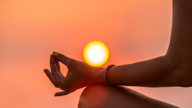 fingers pinched in a meditation with sun in the background