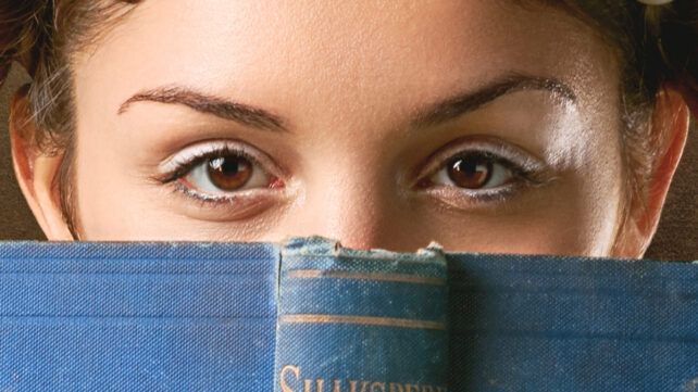 A young person's brown eyes peering over the top of an open book
