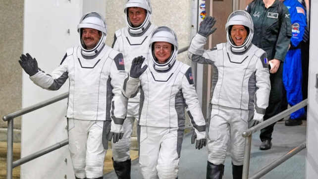 Four astronauts in white spacesuits walking out to board