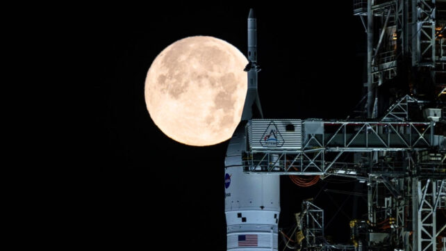 A full moon looking huge, directly behind NASA's SLS and Origin