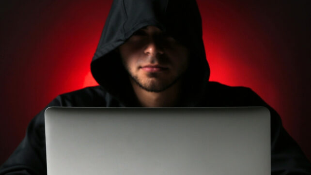 Hacker using a laptop in red light on dark background
