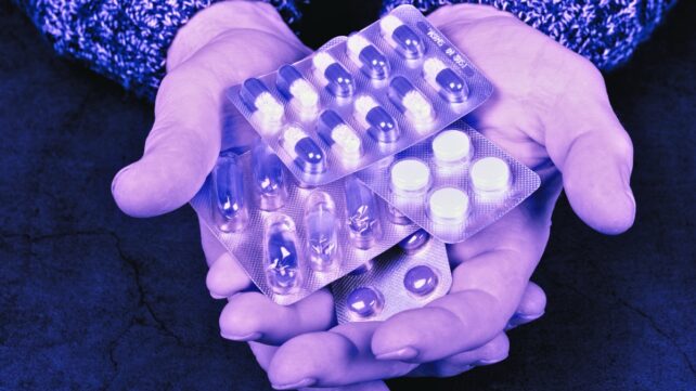 Hands holding blister packs of medication, with a purple tone