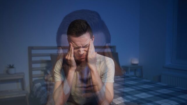 Man sitting on bed holding head in pain