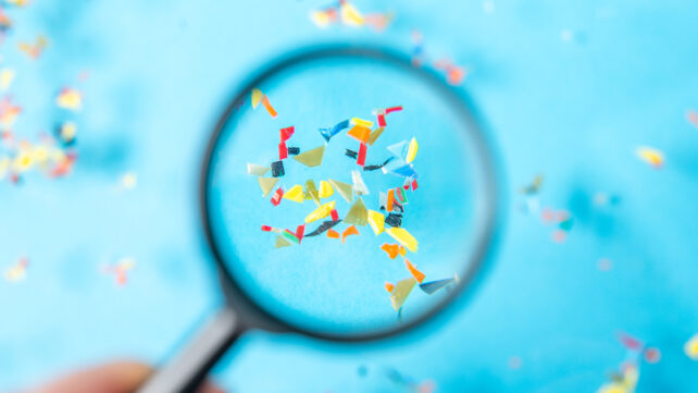 Hand holding magnifying glass reveals enlarged microplastic particles