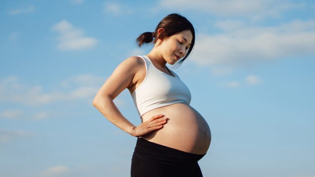 Portrait of pregnant Asian woman relaxing in park