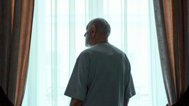 Older Man Standing by the Window Looking Outside