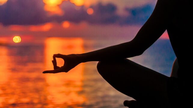 A high contrast image showing a silhouetted human meditating by the ocean at sunset