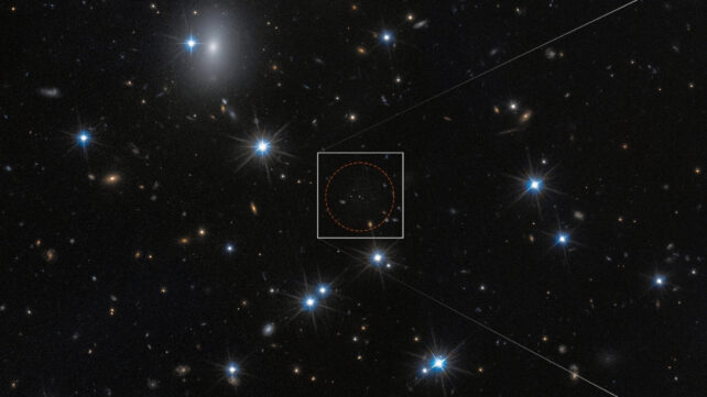 A field of space with a dozen white foreground stars and a number of small, yellow background galaxies. An unremarkable area at centre is outlined with a dashed circle surrounded by a white box.