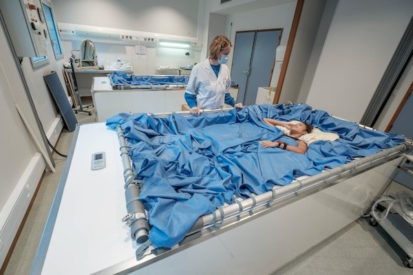 A doctor standing next to a patient in a large bed 