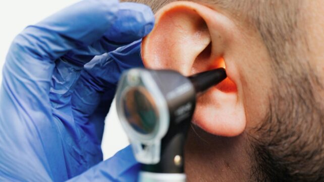 Close up of a gloved hand holding a medical device near a patient's ear