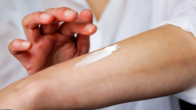 Close up of a person wearing a white shirt applying cream to their arm