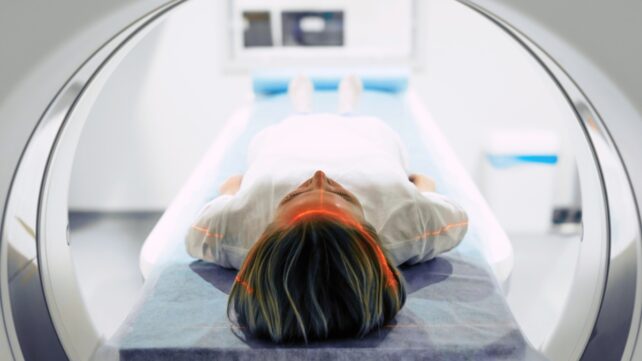 A view from behind an MRI machine, showing a patient ready to enter the scanner