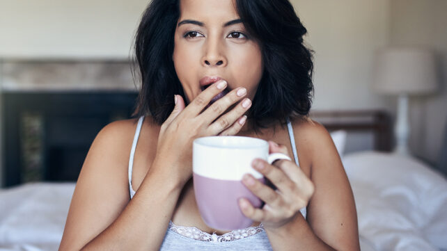 Shot of a young woman yawning while having coffee