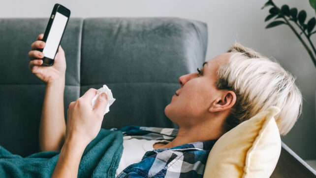 woman laying on the sofa with her phone and a tissue