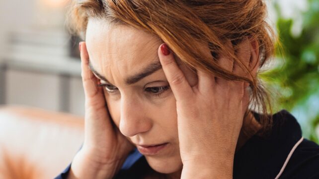 Woman holding her temples with a tense expression, representing stress and nervous system overload