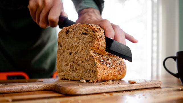A man's hands, cutting a loaf of bread into slices