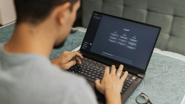 Overhead view of a man typing on a laptop, using an AI chatbot