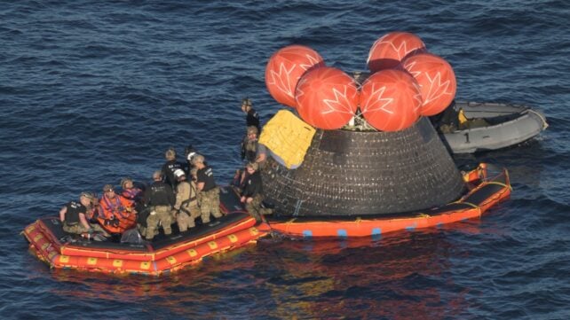 Astronauts and supporting crew on a raft after the Orion spacecraft's splashdown