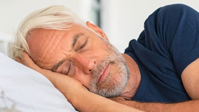 An older man with white hair sleeping during the day